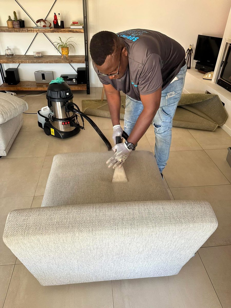 Soum brosse le coussin d'un canapé beige, aspirateur professionnel branché derrière lui
