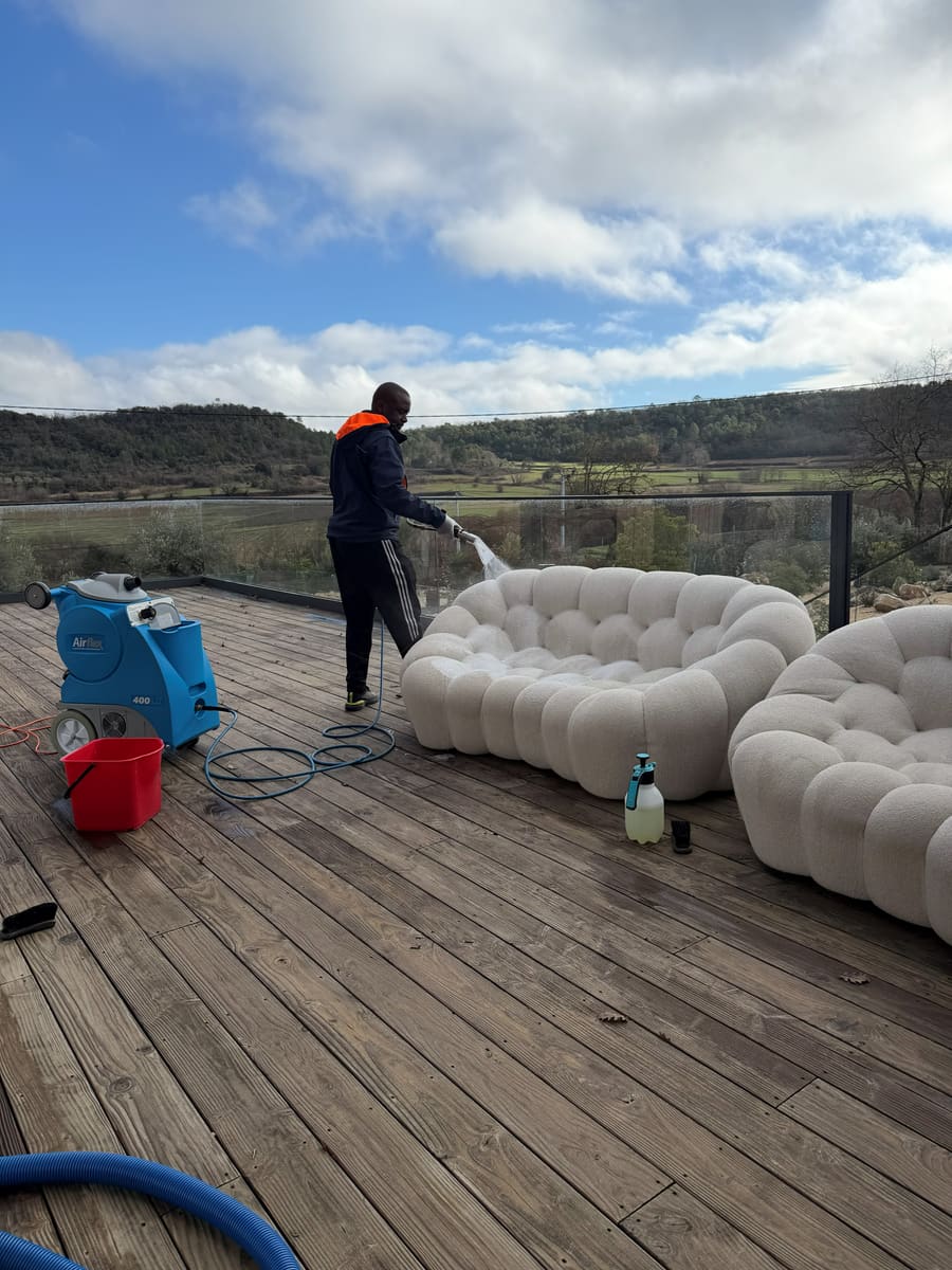 Canapé clair traité sur une terrasse en bois face aux collines, machine et flexible au sol