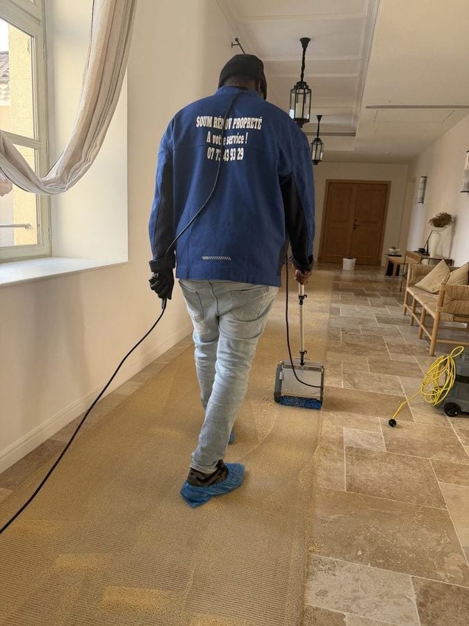 Soum, de dos, tire la monobrosse dans un couloir dallé de travertin