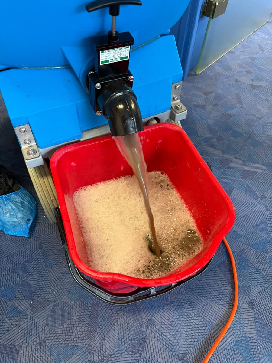 Eau brune rejetée par l'injecteur-extracteur dans un bac rouge, posé sur une moquette bleue