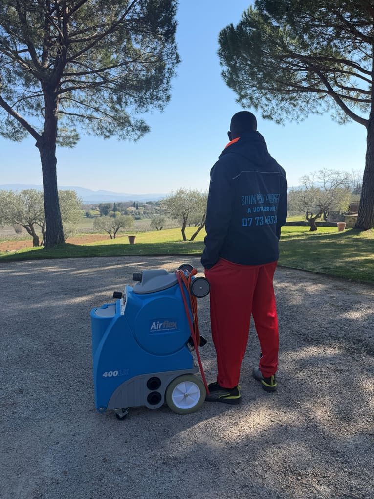 Intervenant poussant la machine sur un chemin bordé de pins, devant un mas