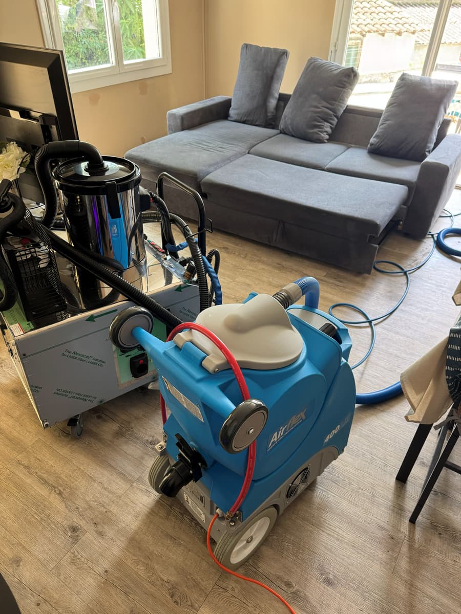 Injecteur-extracteur et aspirateur professionnel installés dans un salon, canapé d'angle gris au fond