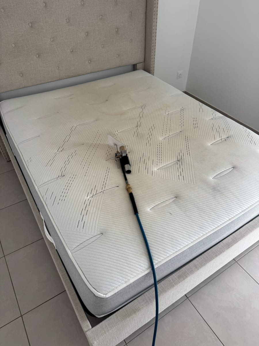 Suceur d'injection-extraction posé sur un matelas blanc, tuyau bleu qui descend au sol