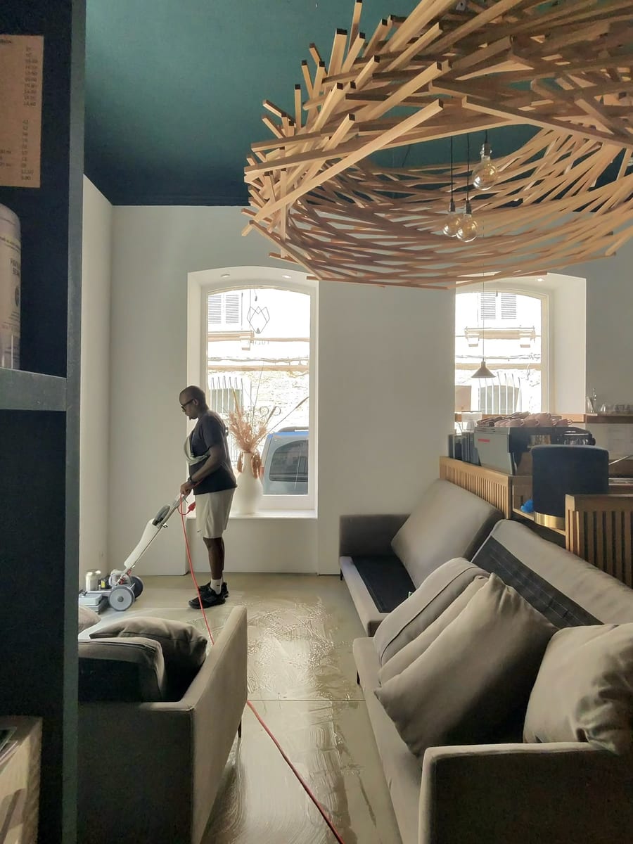 Soum passe la monobrosse sur le sol d'un café, banquettes grises et plafond bleu canard