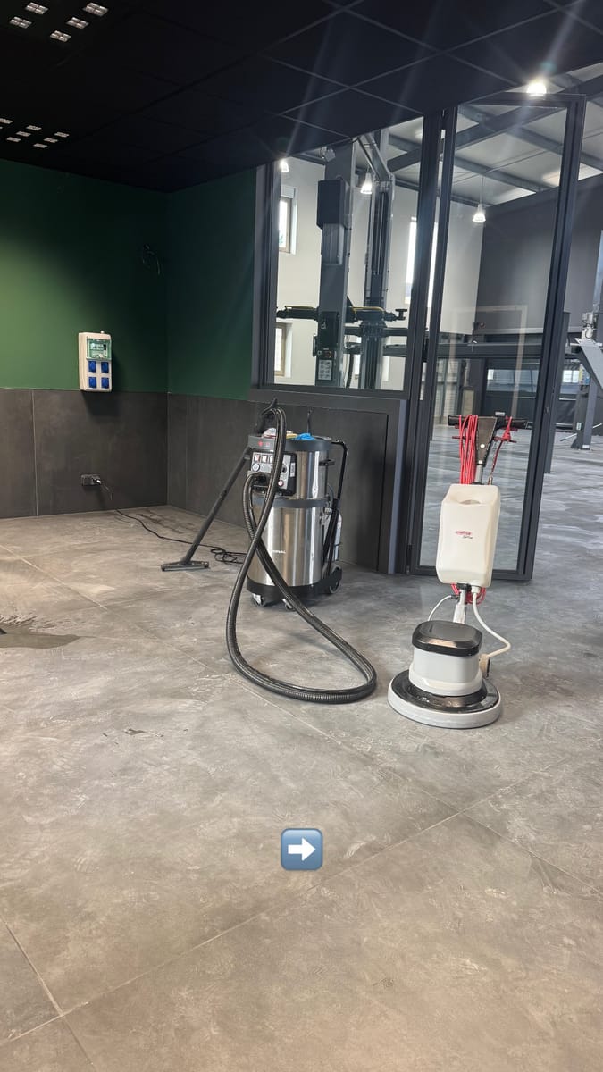 Monobrosse et aspirateur professionnel posés sur le sol carrelé d'un local commercial, cloisons vitrées au fond