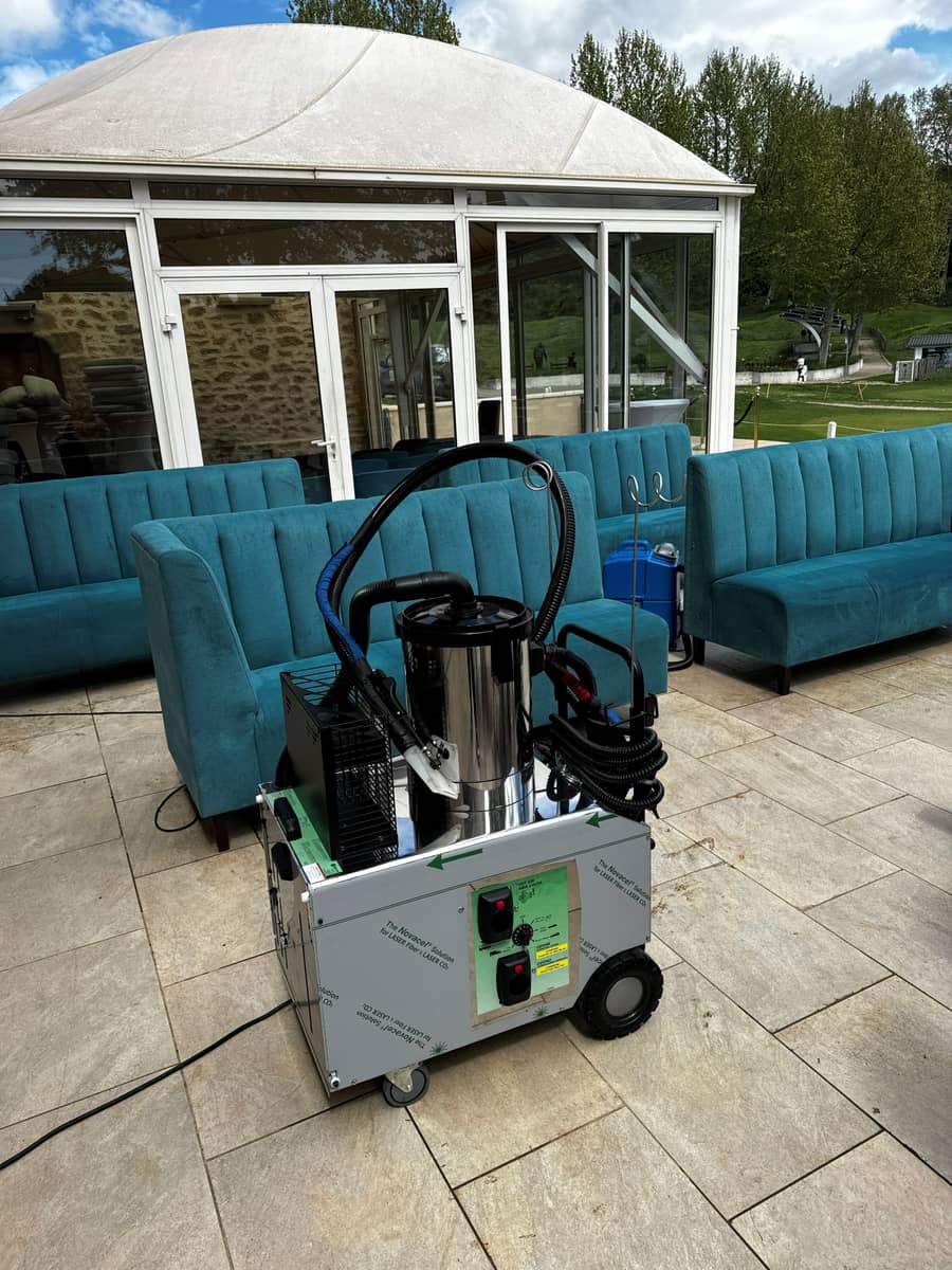 Nettoyeur vapeur professionnel posé sur une terrasse en travertin, banquettes en velours bleu et véranda au fond