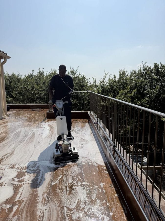 Soum passe la monobrosse sur une terrasse en bois couverte de mousse, garde-corps au fond