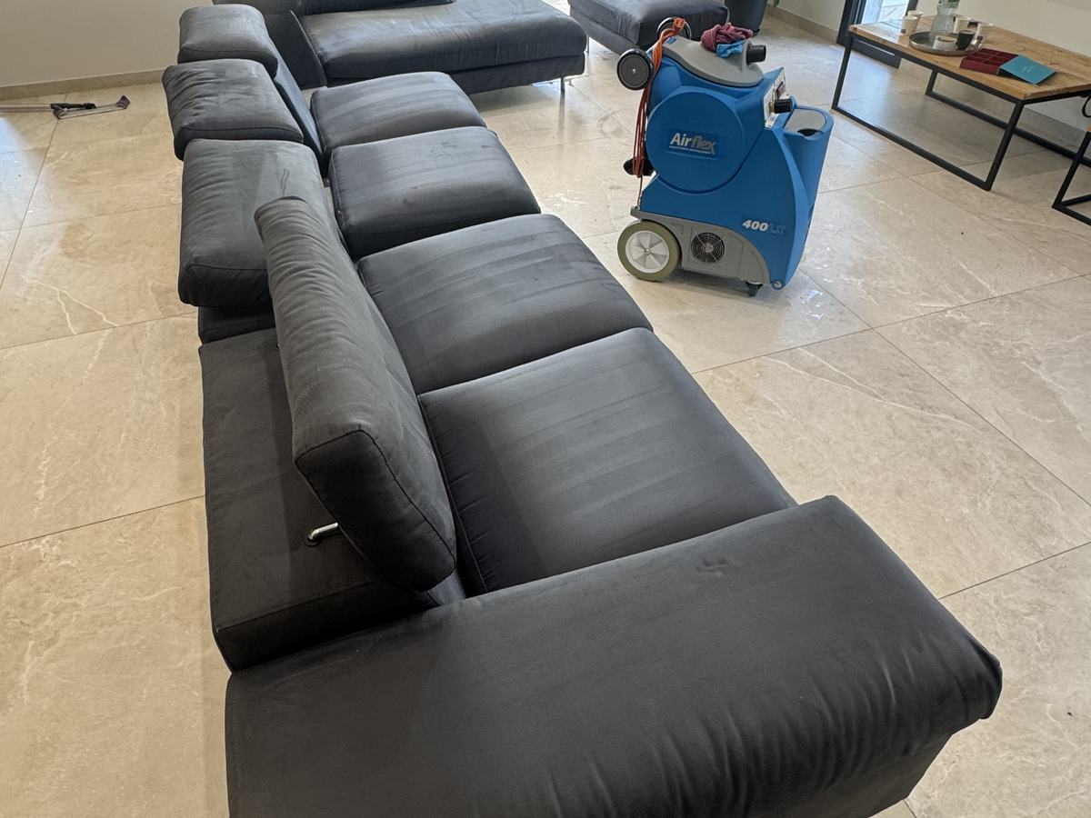 Grand canapé en cuir noir repris, l’injecteur-extracteur encore posé derrière lui