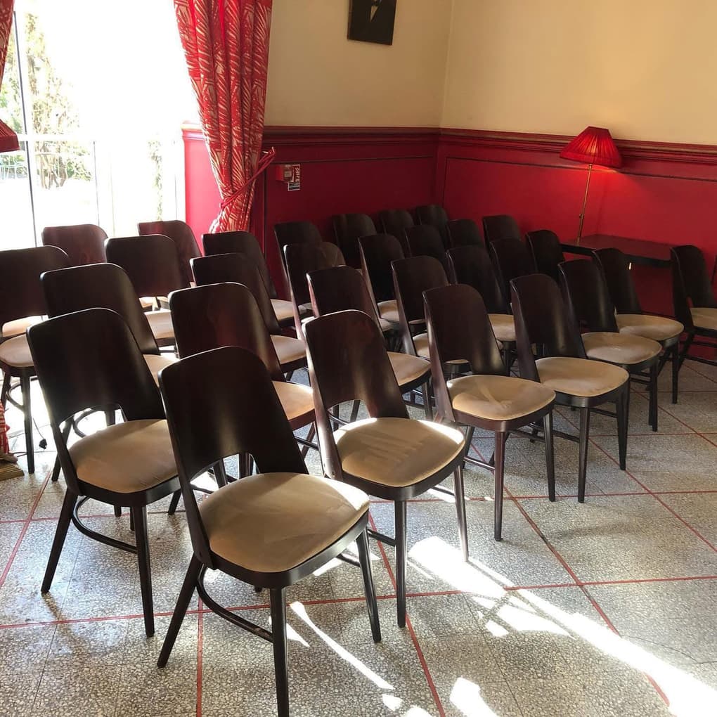 Chaises bistrot rangées en rangs dans une salle à soubassement rouge, sol en granito