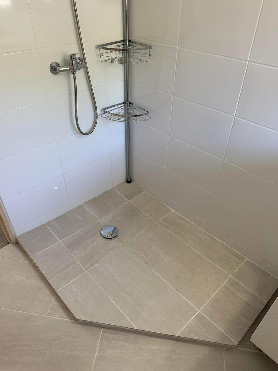 Douche à l'italienne nettoyée, receveur carrelé beige, faïence blanche et robinetterie chromée