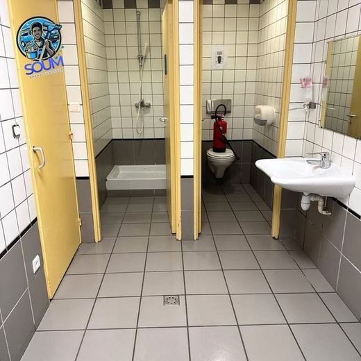 Les mêmes douches collectives après nettoyage, sol carrelé gris uniforme et faïence claire