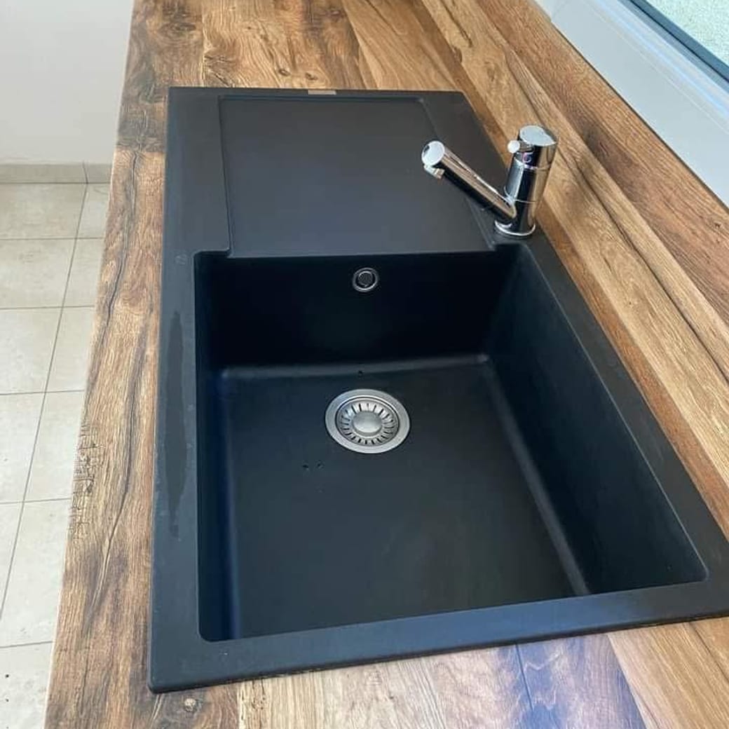Évier en granit noir nettoyé, bonde inox et mitigeur chromé sur un plan de travail imitation bois