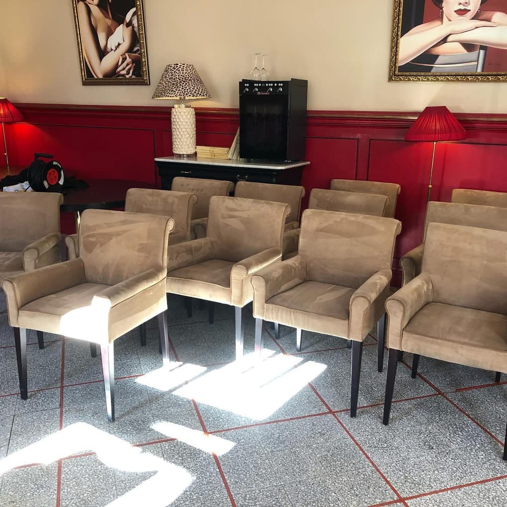 Fauteuils en velours beige alignés dans une salle à soubassement rouge, sol en granito
