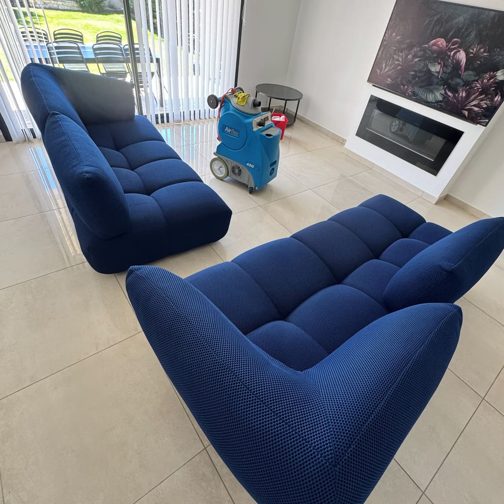 Deux fauteuils bas en maille bleue nettoyés dans un séjour, injecteur-extracteur au fond