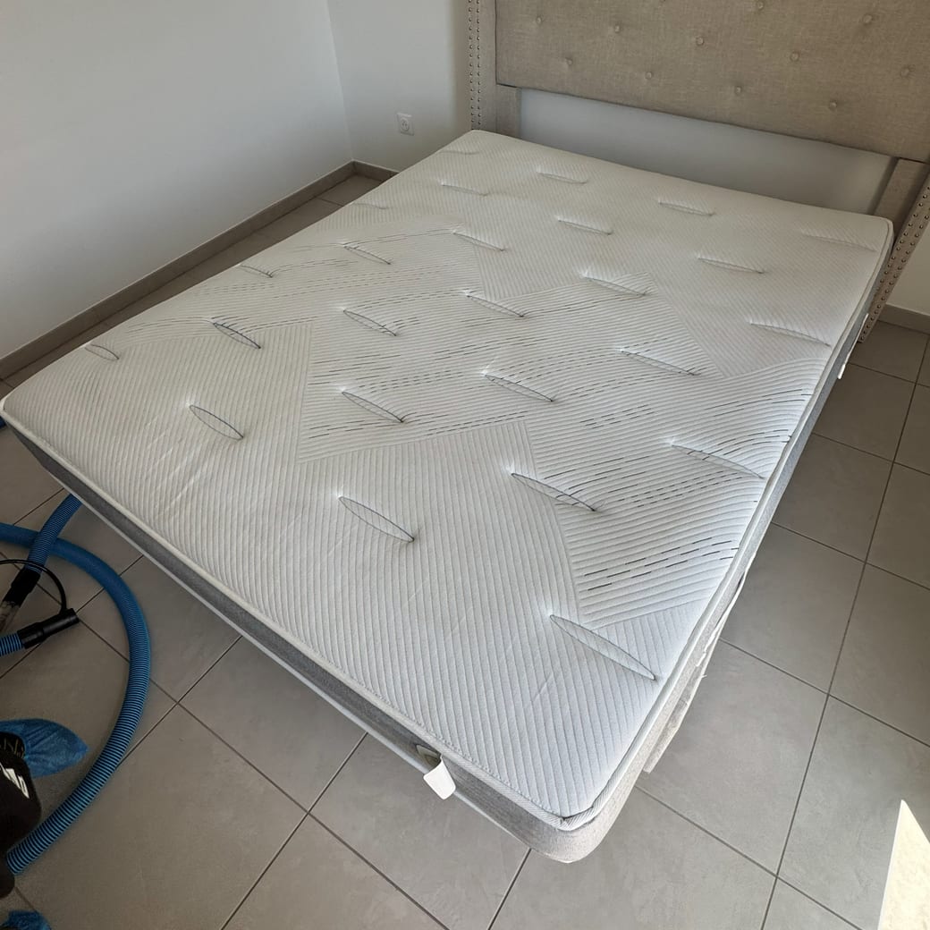 Matelas blanc traité et remis sur son sommier, tête de lit capitonnée, tuyaux de la machine au sol