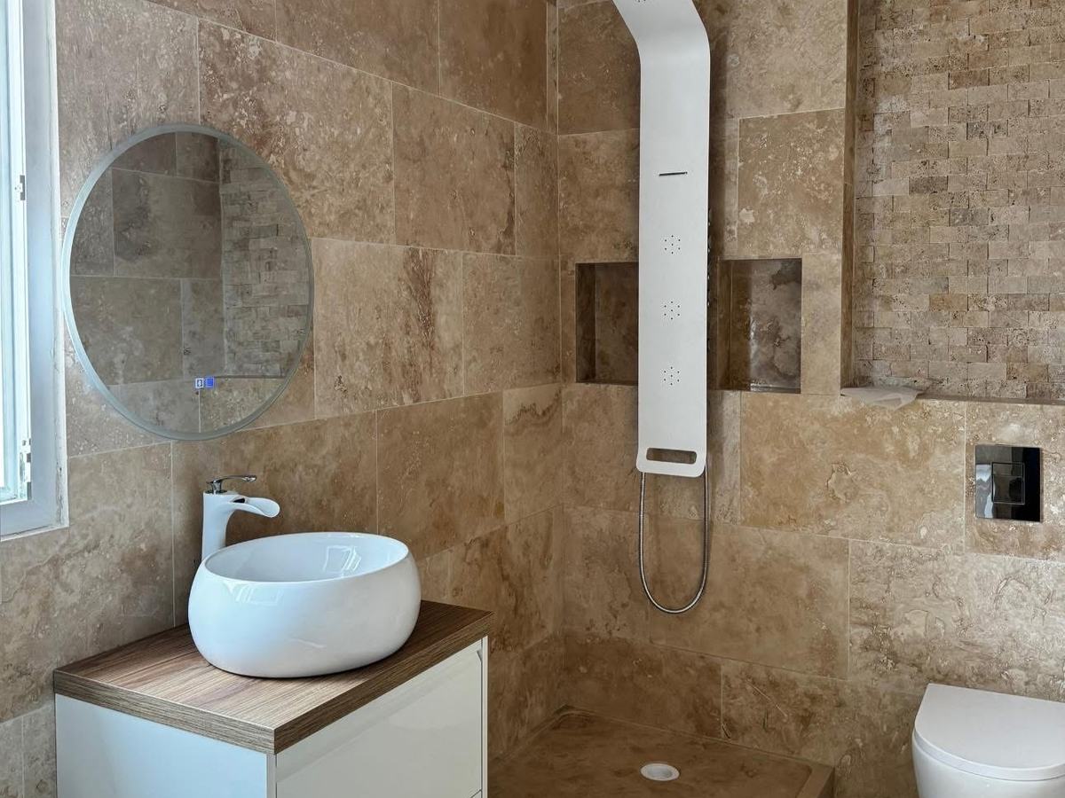 Salle de bain en travertin après remise en état, vasque blanche et colonne de douche