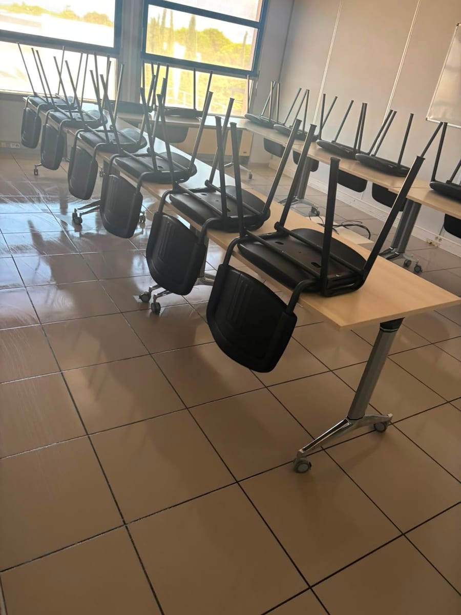 Salle aux chaises noires relevées sur les tables, sol carrelé lavé et brillant