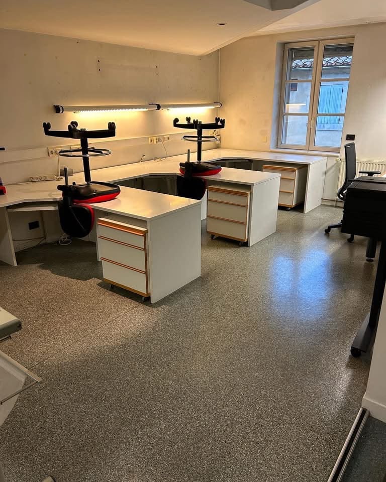 Salle de prothèses dentaires au sol granito nettoyé, plans de travail blancs et articulateurs rouges