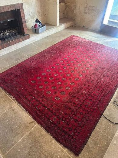 Le même tapis persan après injection-extraction, rouge franc et motifs nets, cheminée au fond