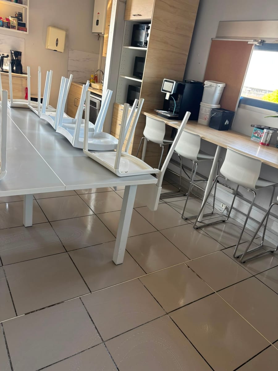 Tisanerie d'entreprise, tabourets et chaises relevés, sol carrelé lavé devant le coin café