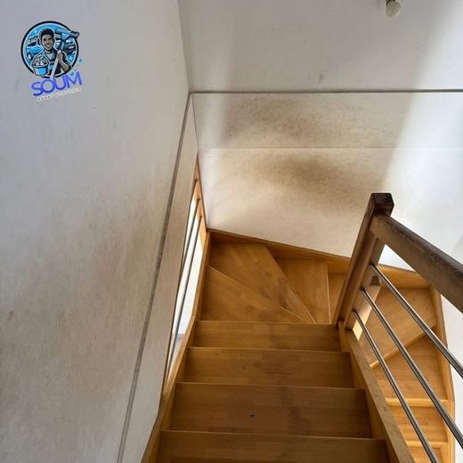 Cage d'escalier en bois dont le mur est couvert de traces brunes étendues