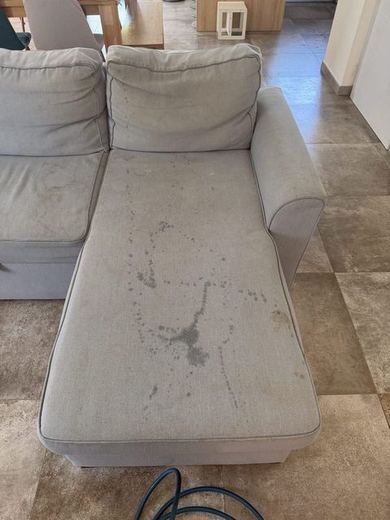 Canapé gris clair à méridienne marqué de coulures et de taches sombres sur son assise