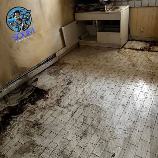 Cuisine vidée dont le sol carrelé est couvert de coulures noires, meubles hauts décrochés