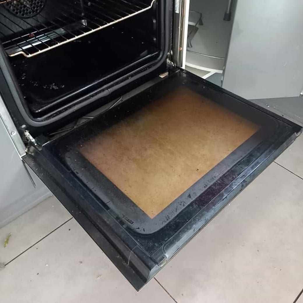 Four ouvert dont la porte vitrée et la lèchefrite sont couvertes de graisse cuite