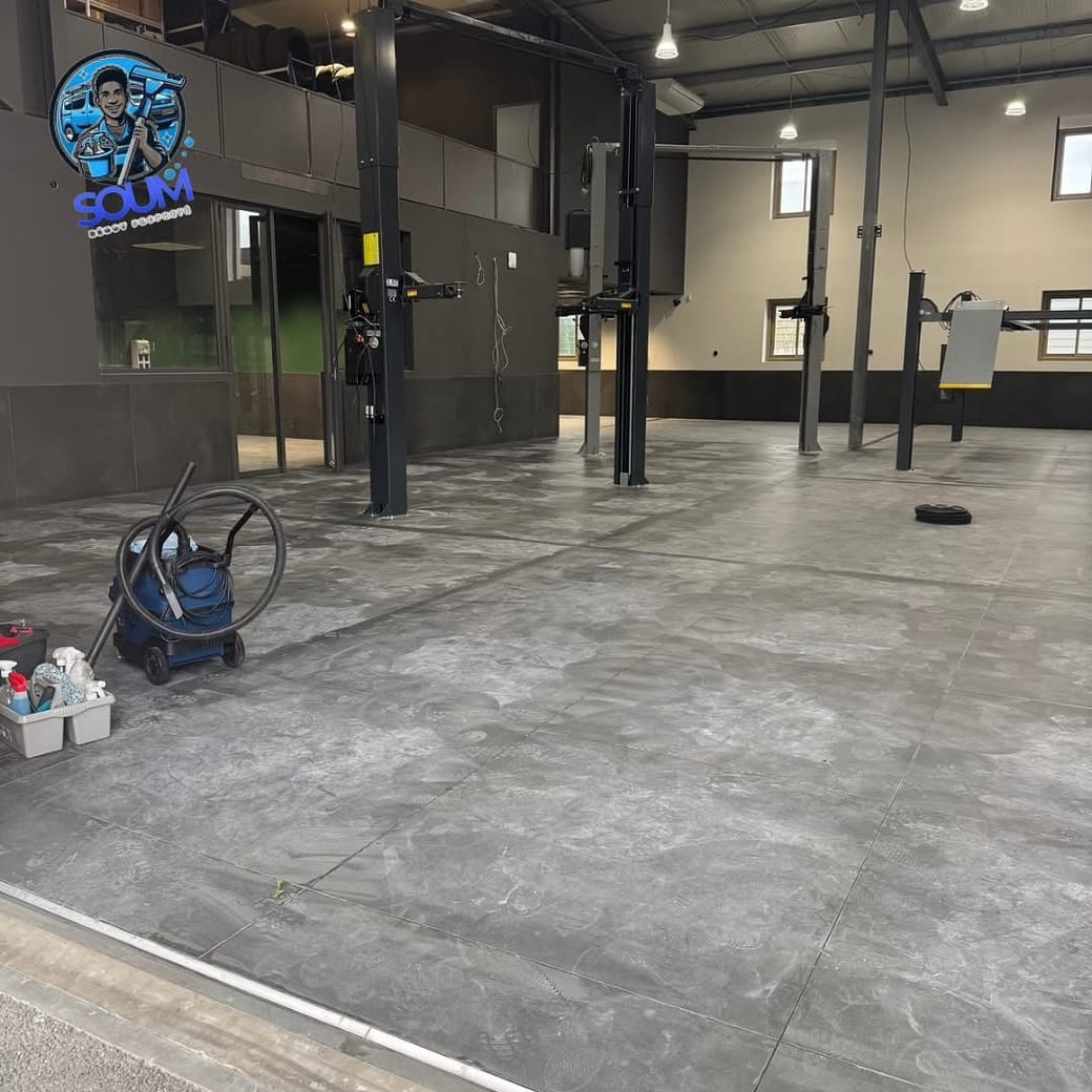 Sol carrelé gris d'un garage automobile voilé de poussière de chantier, aspirateur professionnel au premier plan