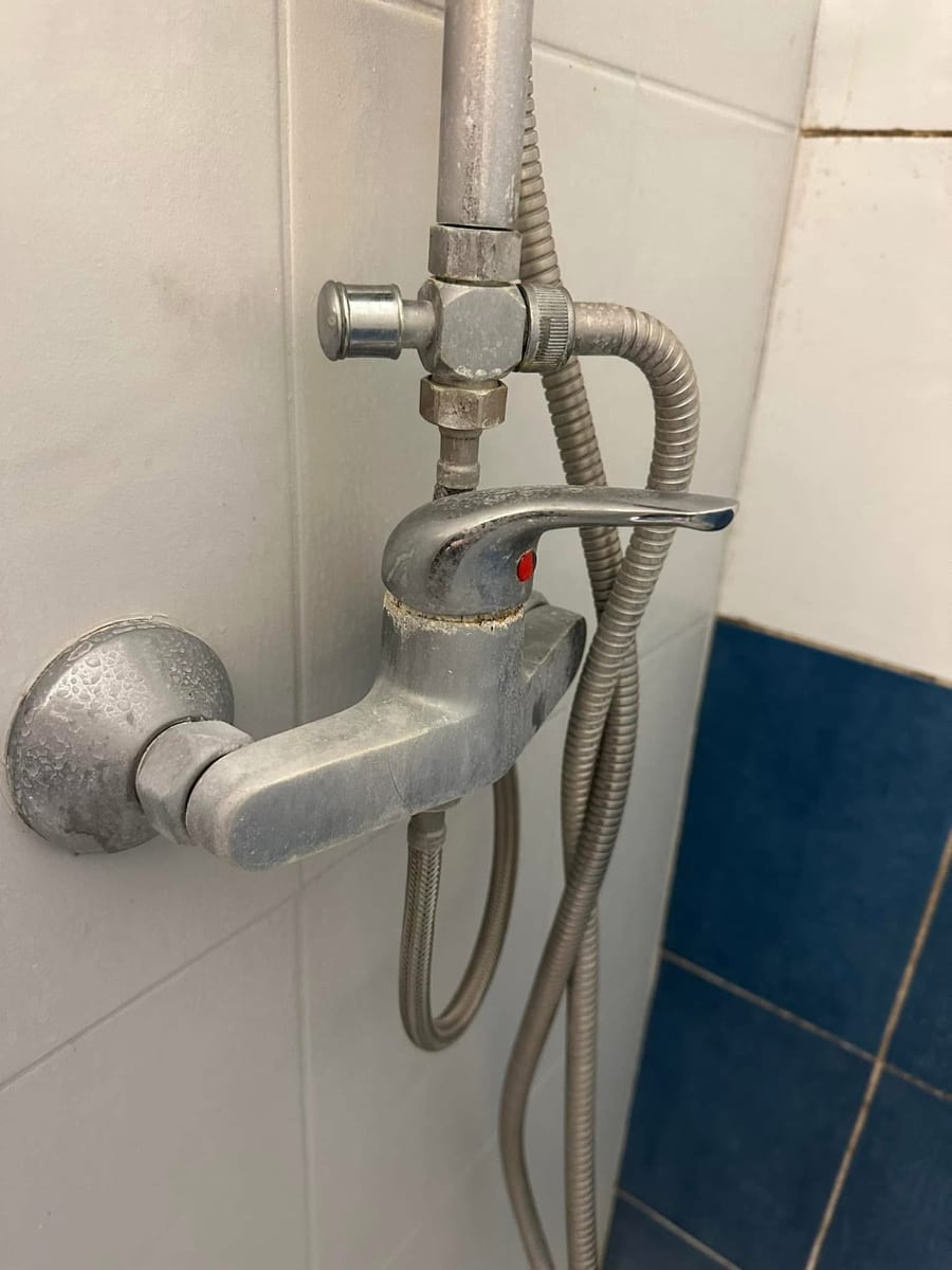 Mitigeur de douche entartré, dépôt blanc épais sur le corps et le flexible, faïence blanche et bleue