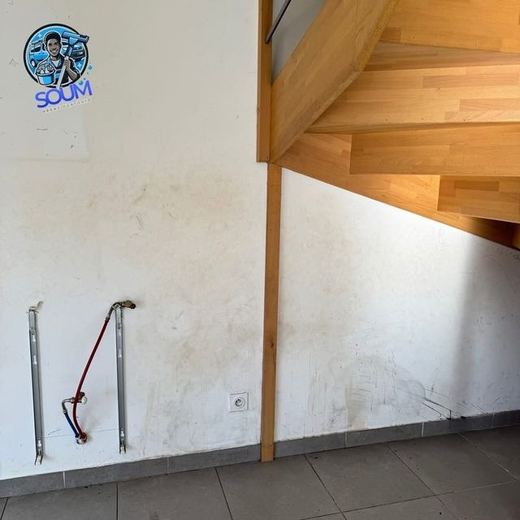 Mur sous un escalier en bois, couvert de coulures ocre et de traces d'humidité
