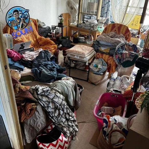 Séjour envahi de vêtements, de sacs et d’objets empilés jusque sur les fauteuils