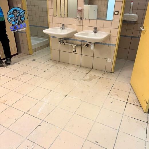 Bloc sanitaire collectif à deux lavabos dont le sol carrelé est terni