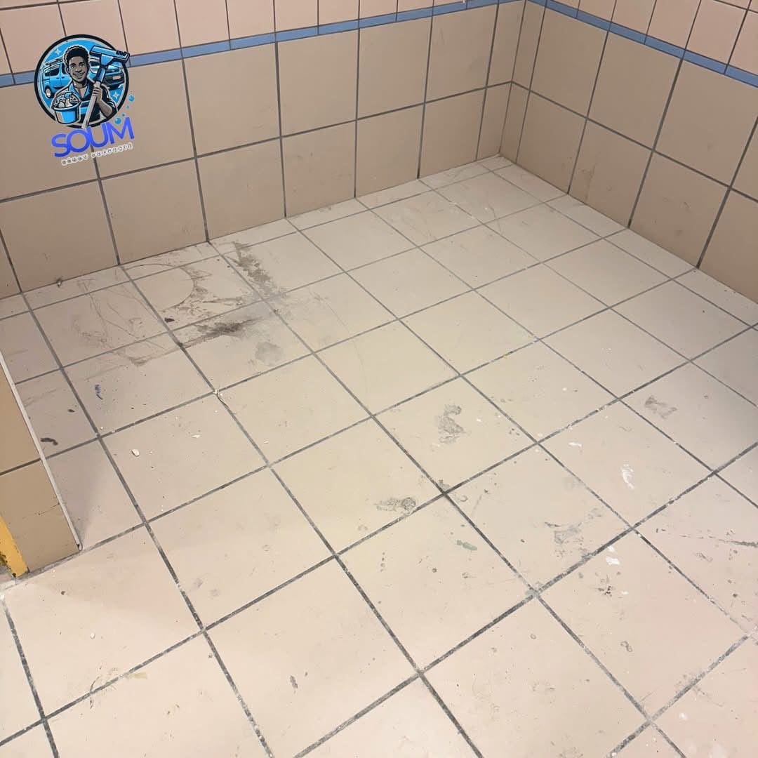 Angle d'une pièce carrelée de cabinet, sol blanc marqué de traînées noires sous un bandeau de faïence bleu