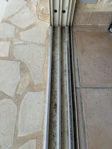 Seuil de baie vitrée : rail d'aluminium encrassé de dépôts noirs et dallage de pierre grisé
