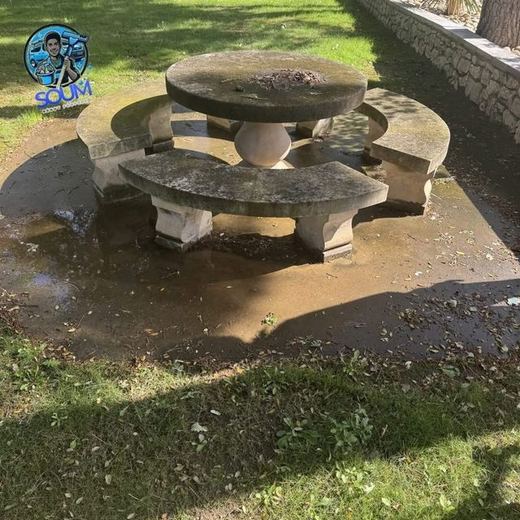 Table de jardin ronde en pierre et ses bancs, verdis par les mousses sur une dalle sombre