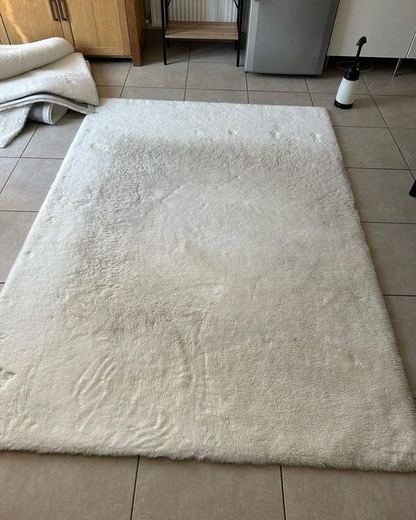 Tapis écru à poils longs posé sur un carrelage, fibres tassées et grisées par endroits