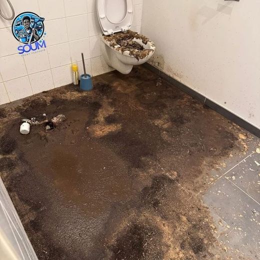 Sanitaire dont la cuvette a débordé et dont le sol est entièrement recouvert de souillures