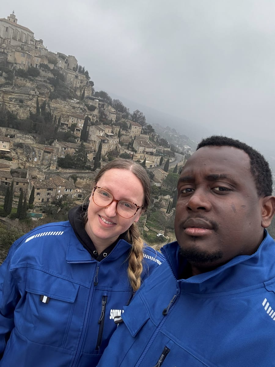 Soum et Cassandra en tenue de travail bleue, portrait pris devant un village perché