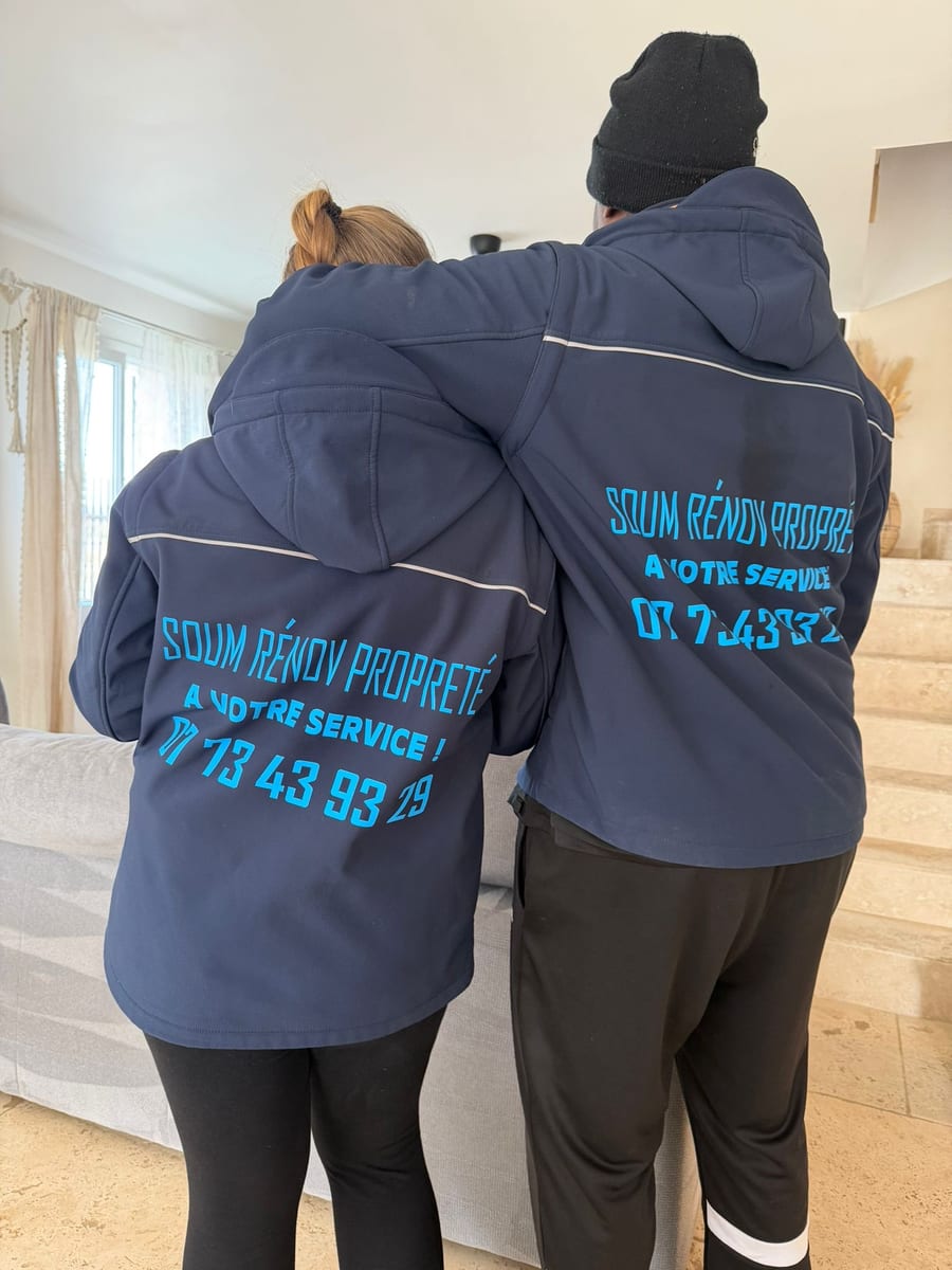 Soum et Cassandra de dos, en veste Soum Rénov Propreté floquée du numéro de téléphone, dans un salon