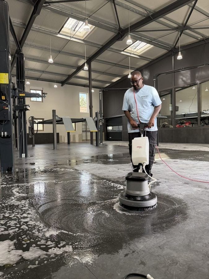 Soum passe la monobrosse sur le sol béton d’un hangar industriel, la mousse au sol