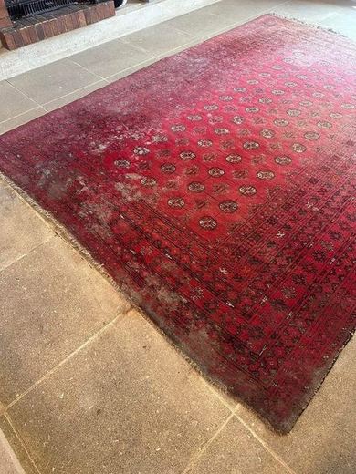 Tapis persan rouge en cours de nettoyage, une moitié déjà ravivée et l’autre encore grisée